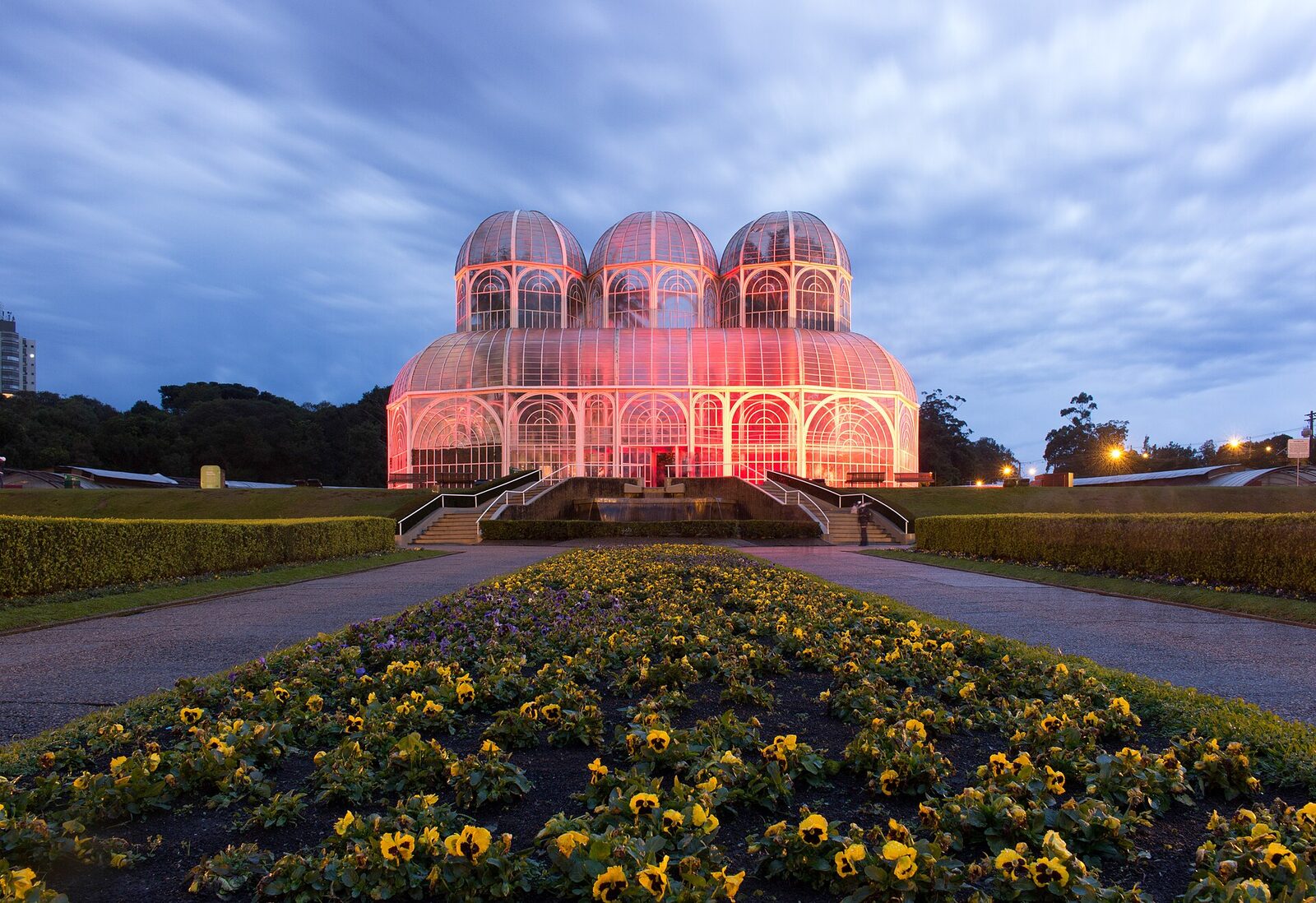Estufa do Jardim Botânico de Curitiba ao anoitecer, com canteiros de flores